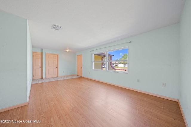 empty room featuring a textured ceiling, light wood-style floors, visible vents, and baseboards