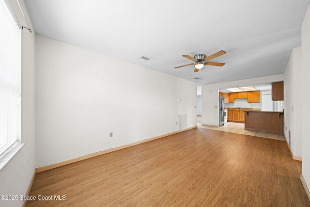 unfurnished living room featuring baseboards, light wood-style floors, visible vents, and ceiling fan