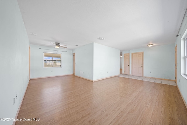 unfurnished room with a ceiling fan, visible vents, light wood finished floors, and baseboards