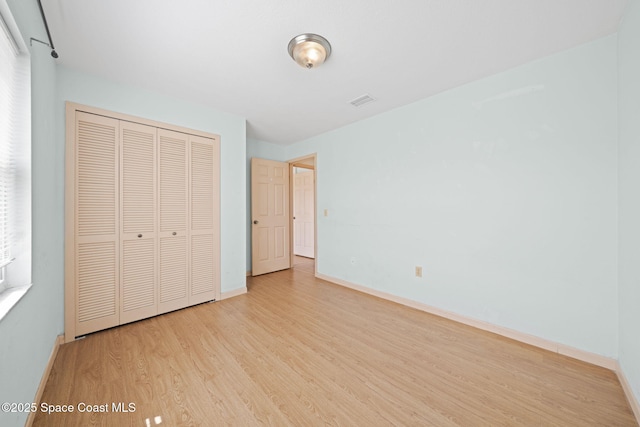 unfurnished bedroom with a closet, baseboards, visible vents, and wood finished floors