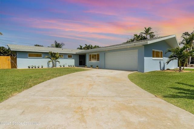 ranch-style home featuring a front lawn, fence, stucco siding, a garage, and driveway