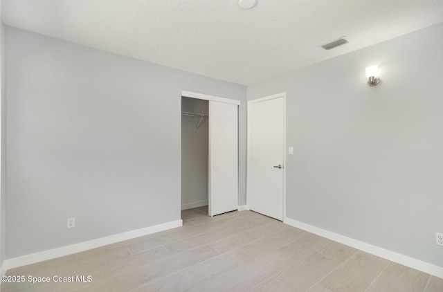 unfurnished bedroom with baseboards, visible vents, a closet, a textured ceiling, and light wood-type flooring