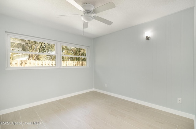 empty room featuring a ceiling fan, light wood-style floors, baseboards, and a textured ceiling