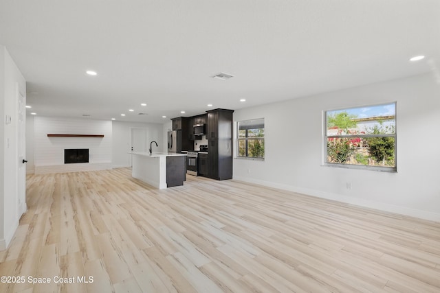 unfurnished living room featuring visible vents, light wood-style flooring, a sink, recessed lighting, and baseboards