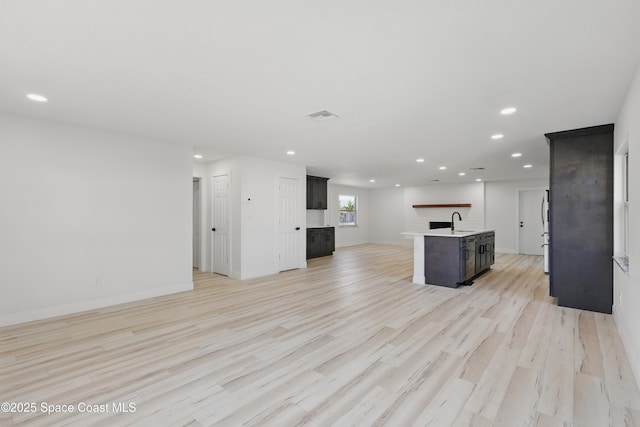 unfurnished living room with light wood finished floors, visible vents, baseboards, recessed lighting, and a sink