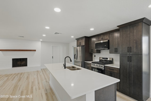 kitchen featuring visible vents, dark brown cabinetry, a center island with sink, stainless steel appliances, and a sink