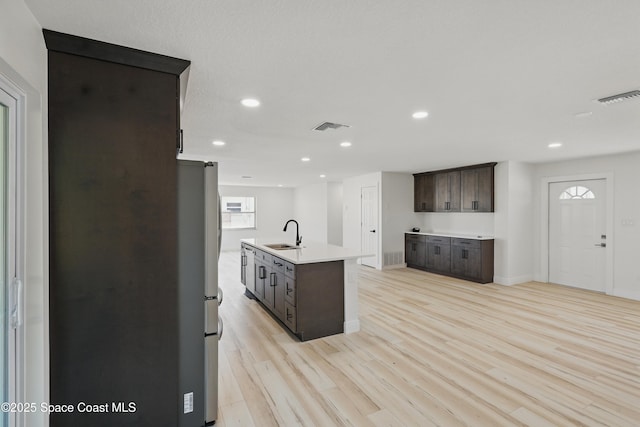 kitchen featuring visible vents, dark brown cabinets, light wood-style floors, and a sink