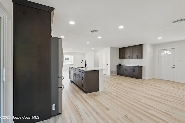 kitchen with a sink, visible vents, light wood-style floors, and dark brown cabinetry