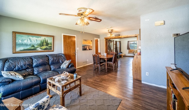 living area with baseboards, a textured wall, dark wood-style floors, a textured ceiling, and a ceiling fan