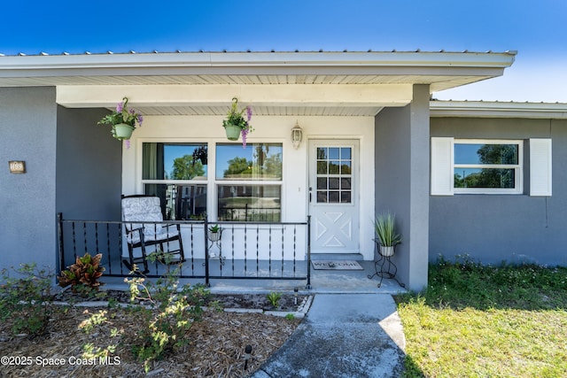 doorway to property with covered porch and stucco siding