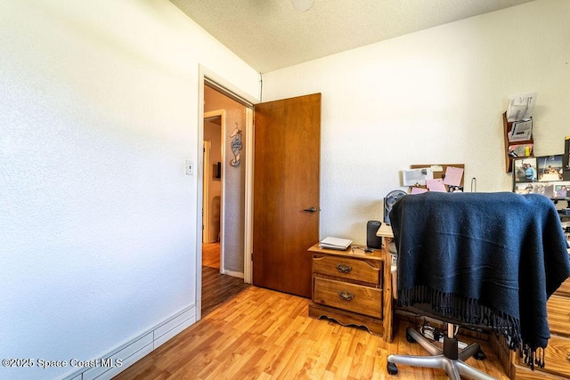 home office featuring light wood-style flooring, a textured ceiling, and baseboards