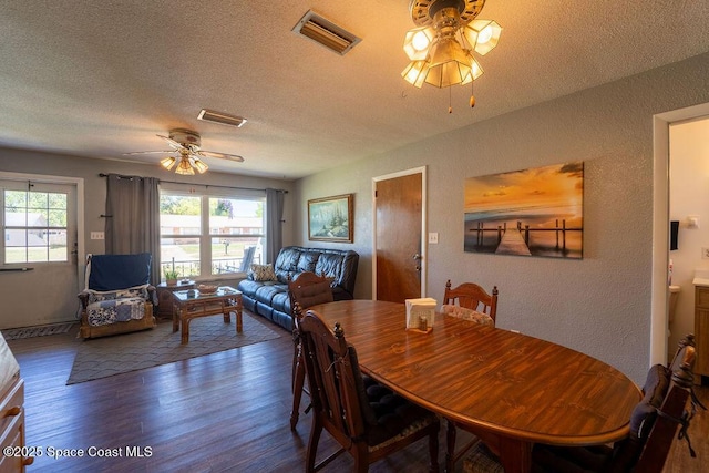 dining room with visible vents, wood finished floors, ceiling fan, and a textured wall