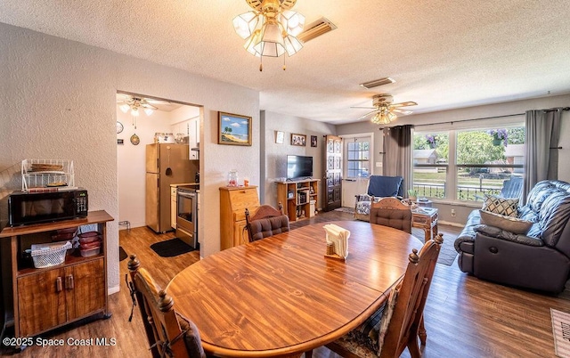 dining area featuring wood finished floors, visible vents, ceiling fan, a textured ceiling, and a textured wall