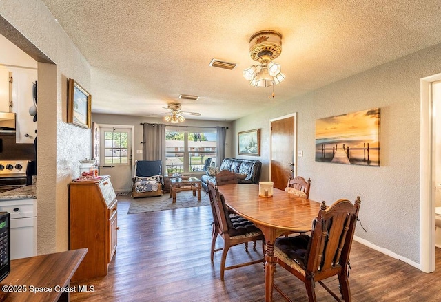 dining area featuring wood finished floors, a ceiling fan, visible vents, a textured ceiling, and a textured wall