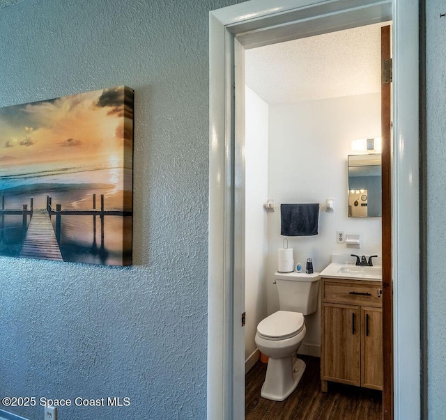 half bath featuring toilet, vanity, a textured wall, and wood finished floors