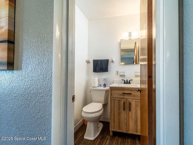 half bath featuring vanity, toilet, wood finished floors, and baseboards