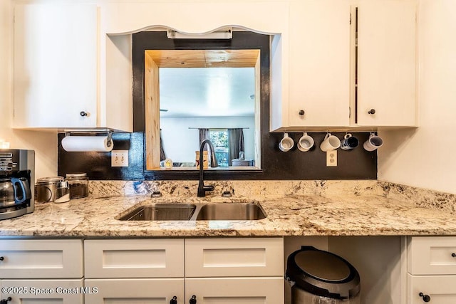 kitchen featuring white cabinets, light stone countertops, and a sink