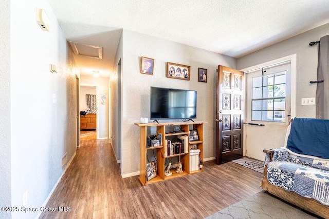 living room with a textured ceiling, attic access, baseboards, and wood finished floors