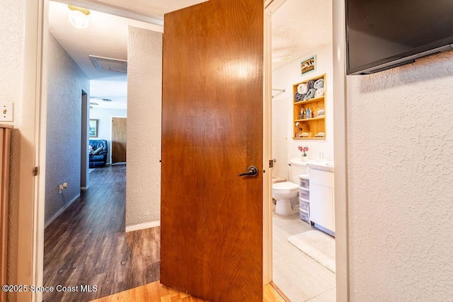 hallway featuring baseboards, wood finished floors, and a textured wall