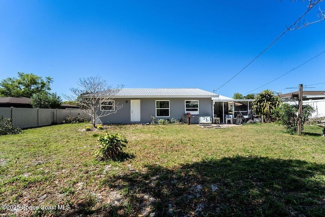 rear view of property with stucco siding, fence, a yard, a sunroom, and metal roof