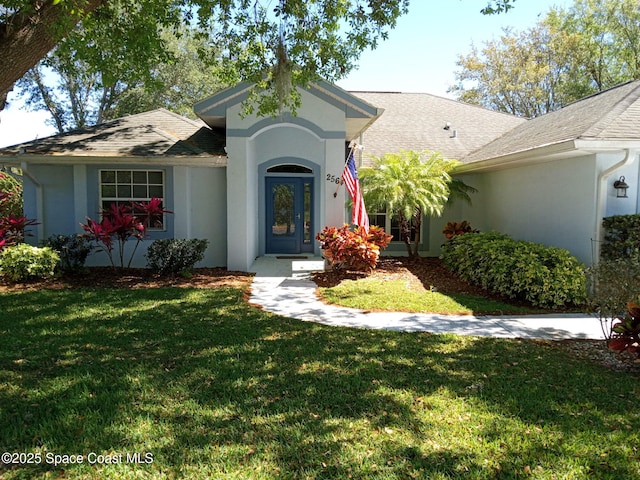 view of front of house with stucco siding, a front yard, and a shingled roof