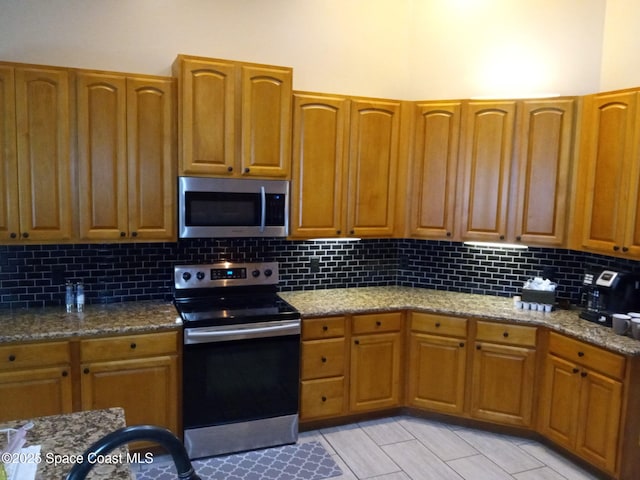kitchen featuring decorative backsplash, dark stone counters, brown cabinetry, and stainless steel appliances