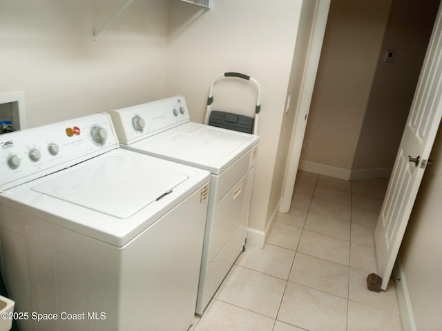 clothes washing area featuring light tile patterned flooring, laundry area, washer and dryer, and baseboards
