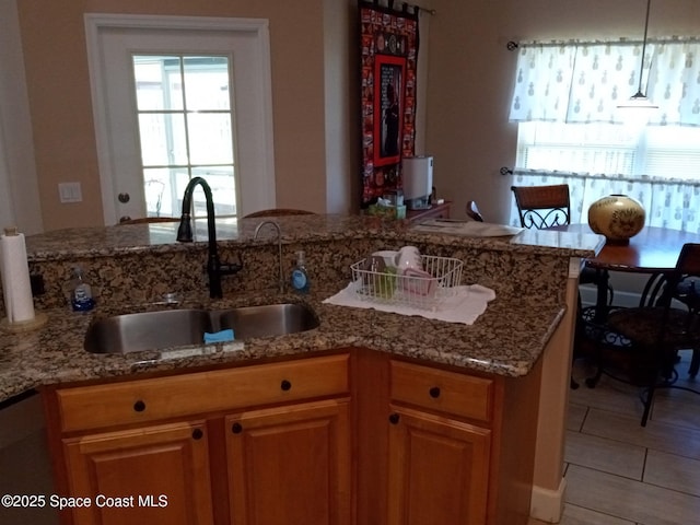 kitchen with a sink, light stone countertops, stainless steel dishwasher, and pendant lighting