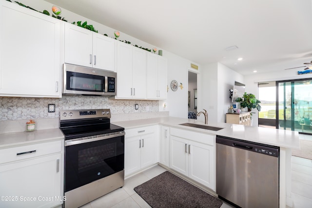 kitchen with a sink, tasteful backsplash, appliances with stainless steel finishes, a peninsula, and light countertops