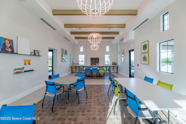 dining area featuring baseboards, a chandelier, beamed ceiling, a high ceiling, and plenty of natural light