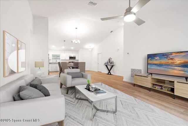 living room with light wood finished floors, visible vents, ceiling fan with notable chandelier, and high vaulted ceiling