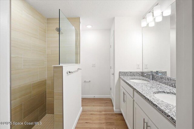 full bathroom featuring baseboards, walk in shower, double vanity, wood finished floors, and a sink
