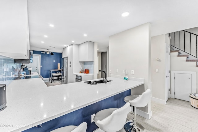 kitchen featuring backsplash, a breakfast bar, light wood-type flooring, white cabinetry, and a sink