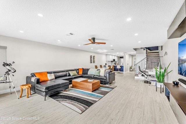 living area with a ceiling fan, visible vents, stairs, a textured ceiling, and light wood-type flooring