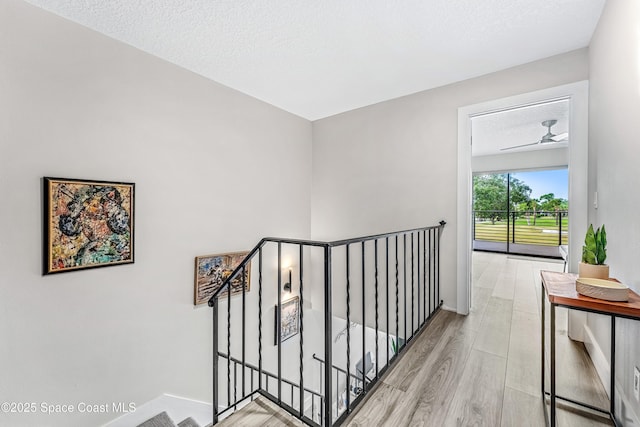 hall with an upstairs landing, a textured ceiling, baseboards, and wood finished floors