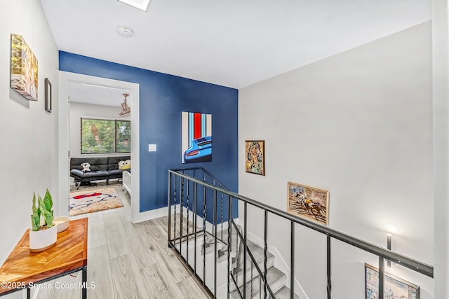 hall with baseboards, an upstairs landing, and light wood finished floors