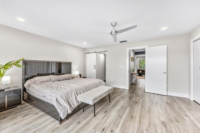 bedroom featuring baseboards, visible vents, light wood finished floors, recessed lighting, and a barn door