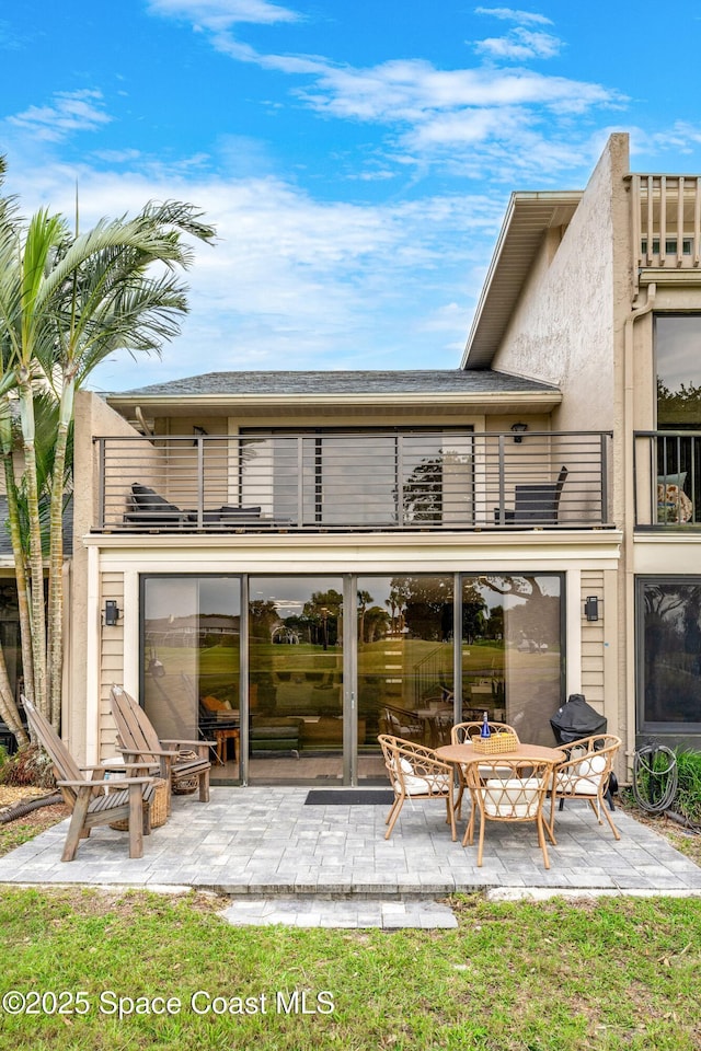 back of house with stucco siding, a patio, and a balcony
