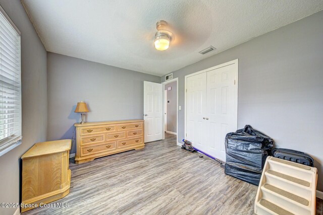bedroom featuring a closet, visible vents, a textured ceiling, and wood finished floors