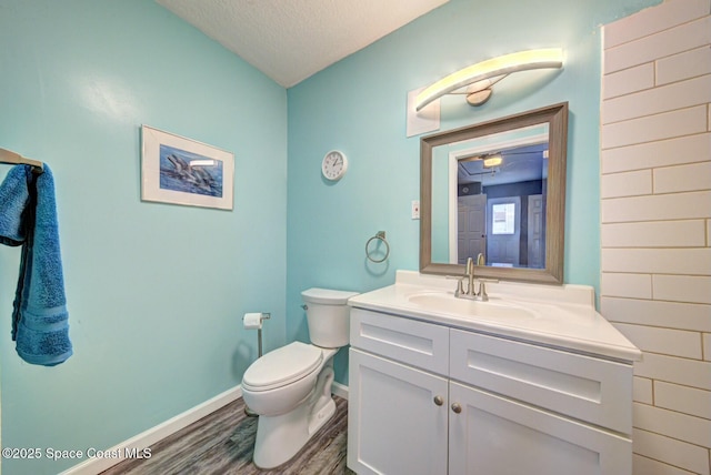 half bathroom with toilet, a textured ceiling, wood finished floors, baseboards, and vanity