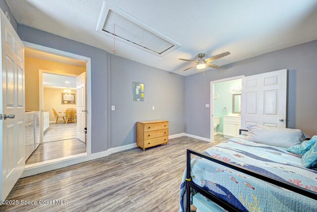bedroom with wood finished floors, baseboards, ensuite bath, attic access, and ceiling fan