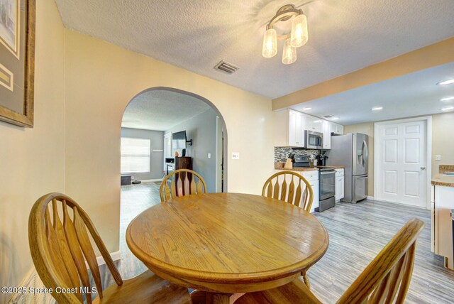dining area with visible vents, light wood-style flooring, a textured ceiling, arched walkways, and baseboards