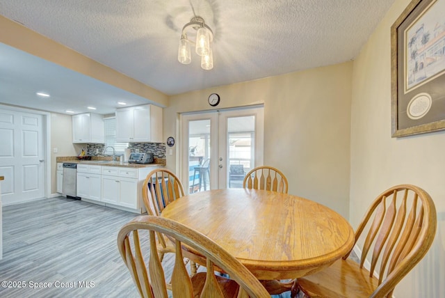 dining space featuring french doors, light wood finished floors, and a textured ceiling