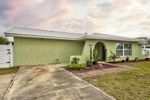 view of front facade featuring stucco siding, metal roof, and a gate