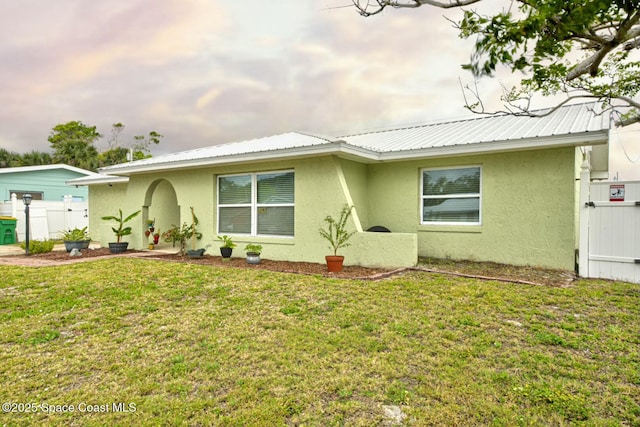 ranch-style home with a front yard, stucco siding, fence, and metal roof