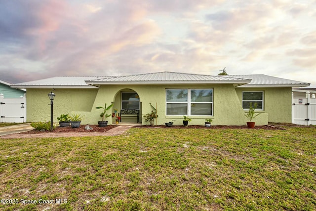 single story home with stucco siding, a gate, a front lawn, and metal roof