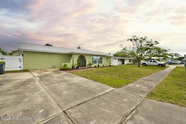 ranch-style house with fence, stucco siding, a front lawn, concrete driveway, and metal roof