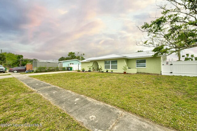 ranch-style home with a front lawn, fence, stucco siding, metal roof, and a gate