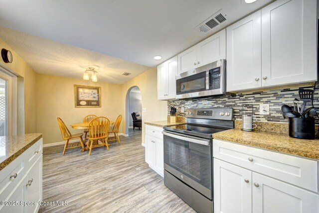 kitchen featuring light wood finished floors, visible vents, decorative backsplash, appliances with stainless steel finishes, and arched walkways
