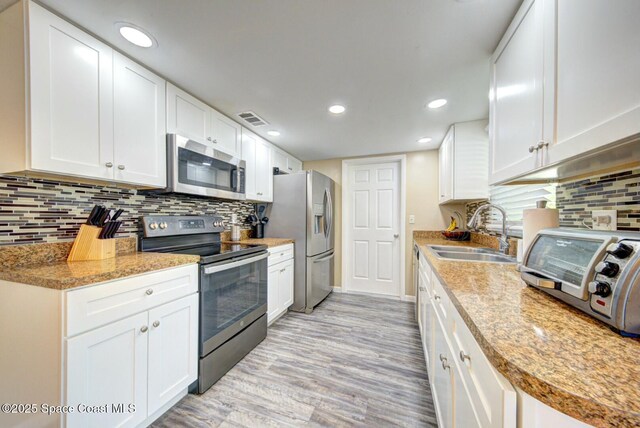 kitchen with recessed lighting, appliances with stainless steel finishes, light wood-style floors, white cabinets, and a sink